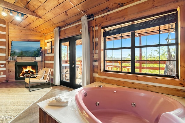 bathroom with lofted ceiling, wooden ceiling, wooden walls, a lit fireplace, and a whirlpool tub