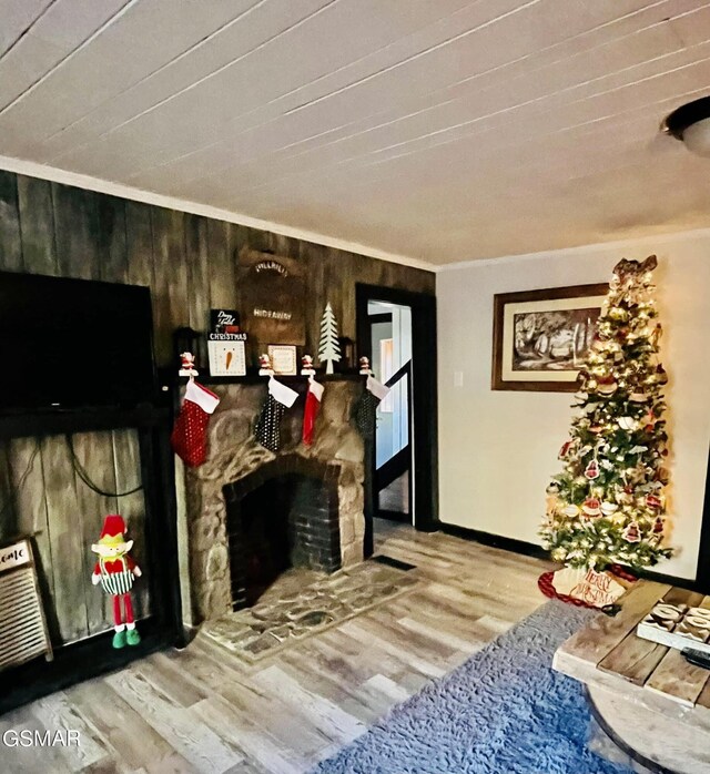 interior space featuring hardwood / wood-style floors, wooden walls, a stone fireplace, and crown molding