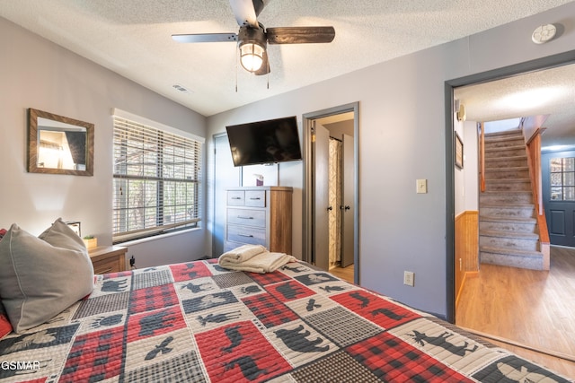 bedroom featuring a ceiling fan, visible vents, a textured ceiling, and wood finished floors