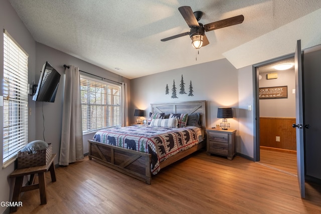 bedroom with wooden walls, a ceiling fan, a wainscoted wall, wood finished floors, and a textured ceiling