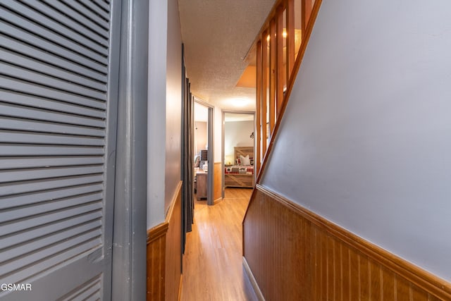 hallway featuring light wood-style flooring, wainscoting, wood walls, and a textured ceiling