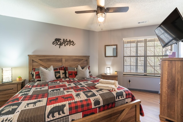 bedroom with a textured ceiling, ceiling fan, light wood-style flooring, and visible vents