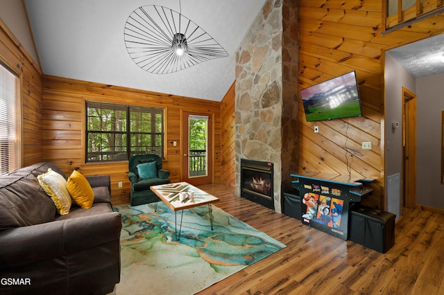 living room with visible vents, wood finished floors, a stone fireplace, wood walls, and high vaulted ceiling