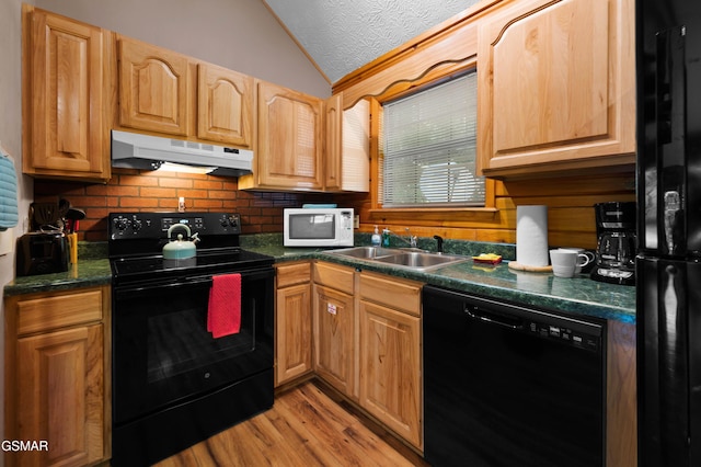 kitchen featuring under cabinet range hood, a sink, vaulted ceiling, black appliances, and dark countertops