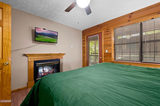 bedroom with a ceiling fan, a glass covered fireplace, a textured ceiling, wood finished floors, and access to outside