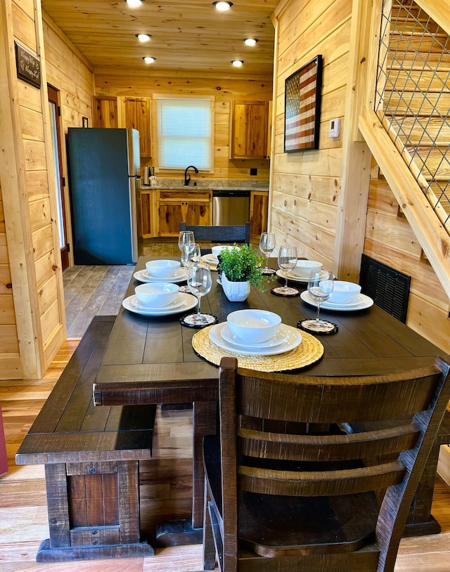 dining space with sink, wooden ceiling, light hardwood / wood-style floors, and wood walls