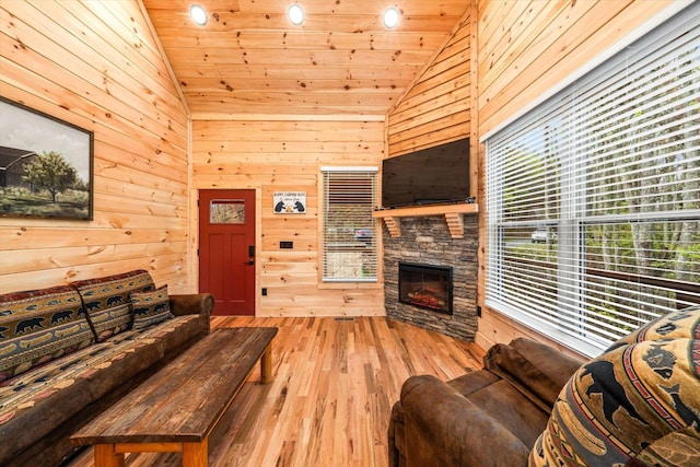 living room with wood ceiling, high vaulted ceiling, wood walls, a stone fireplace, and light wood-type flooring