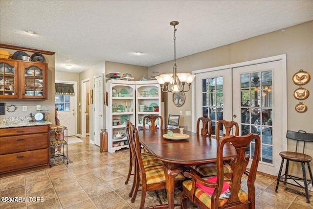 dining room featuring french doors, a textured ceiling, and an inviting chandelier