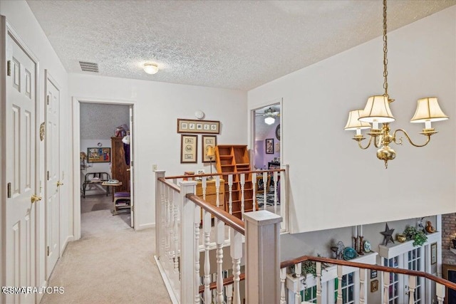 hallway featuring light colored carpet, a textured ceiling, and a notable chandelier