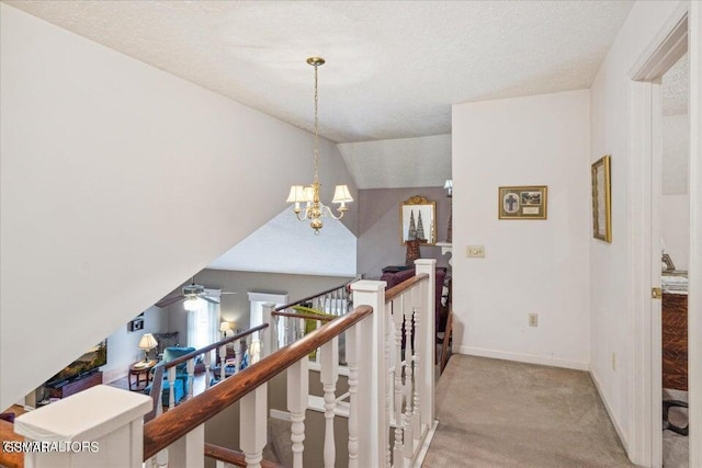 hallway featuring a textured ceiling, light carpet, vaulted ceiling, and an inviting chandelier