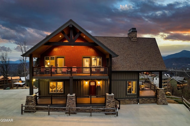 710 Wiley Oakley Dr, Gatlinburg, TN 37738 - back of house at dusk featuring a balcony, board and batten siding, a mountain view, a shingled roof, and a chimney