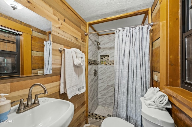 bathroom with a shower with curtain, sink, wooden walls, toilet, and a textured ceiling