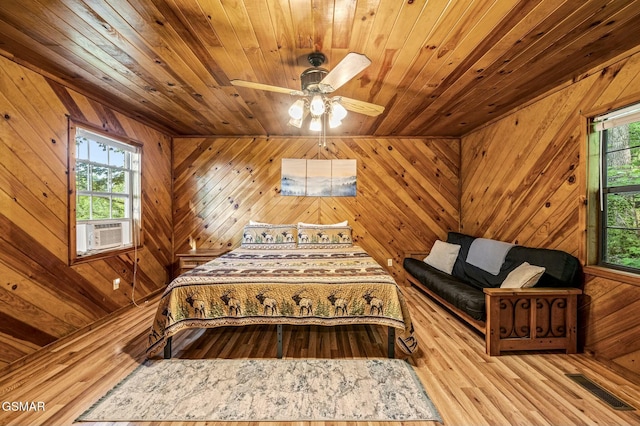 bedroom featuring cooling unit, wooden walls, light hardwood / wood-style flooring, ceiling fan, and wood ceiling