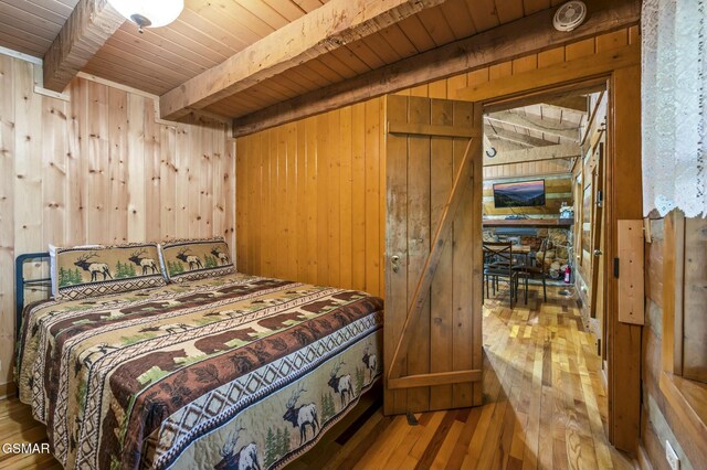 bedroom featuring beamed ceiling, wood walls, wooden ceiling, and hardwood / wood-style floors