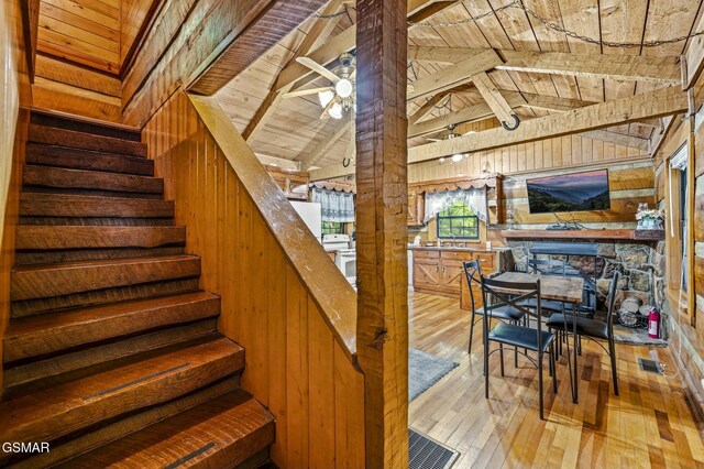 stairway with wooden ceiling, wooden walls, hardwood / wood-style flooring, vaulted ceiling with beams, and ceiling fan