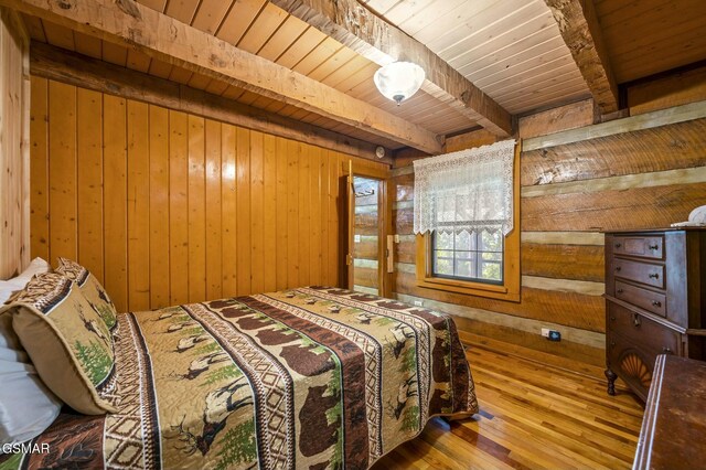 bedroom with beam ceiling, wood walls, hardwood / wood-style floors, and wood ceiling