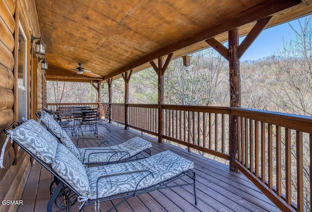 wooden deck with a forest view, outdoor dining space, and a ceiling fan