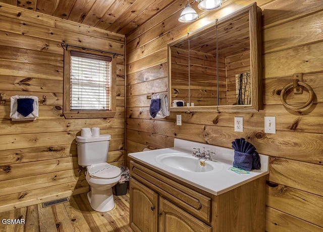 bathroom with visible vents, wood walls, toilet, wood finished floors, and vanity