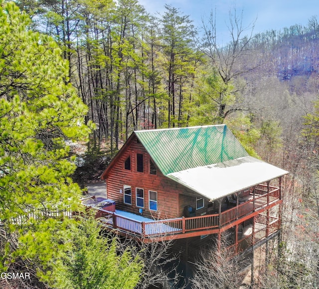 rear view of property featuring metal roof, a wooded view, and a wooden deck