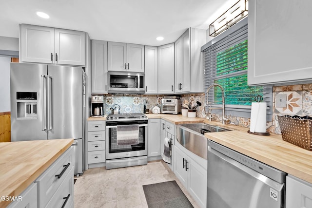 kitchen with sink, stainless steel appliances, wooden counters, and tasteful backsplash