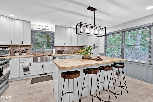 kitchen featuring a center island, stainless steel appliances, wood counters, a breakfast bar area, and white cabinets