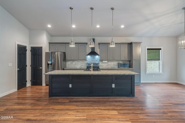 kitchen featuring wall chimney exhaust hood, gray cabinets, an island with sink, appliances with stainless steel finishes, and tasteful backsplash