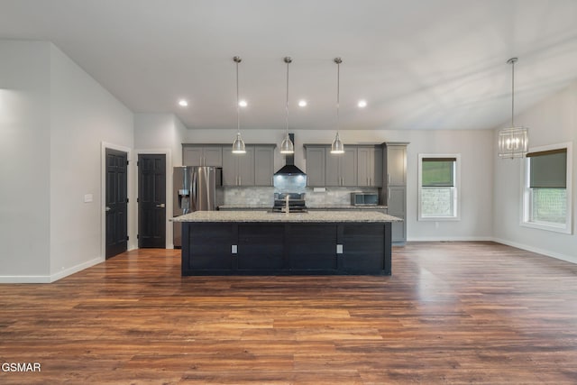 kitchen with gray cabinets, wall chimney exhaust hood, a kitchen island with sink, dark wood-style floors, and decorative backsplash