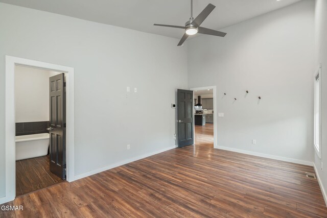 unfurnished bedroom with high vaulted ceiling, wood finished floors, baseboards, and ensuite bath