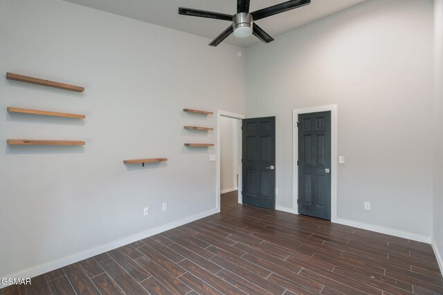 unfurnished room with a ceiling fan, baseboards, a high ceiling, and dark wood-style floors