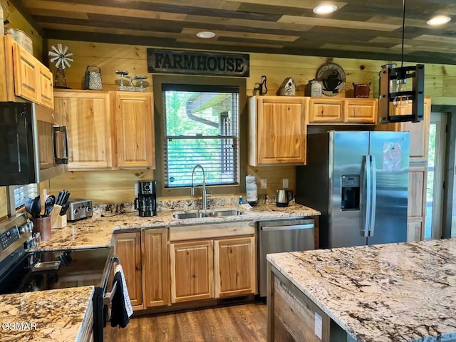 kitchen featuring wooden walls, light stone counters, wood finished floors, stainless steel appliances, and a sink