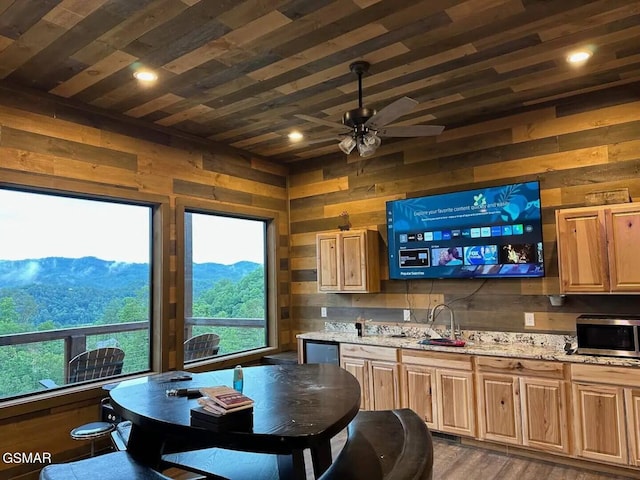 kitchen featuring light stone counters, wooden walls, a sink, wood ceiling, and stainless steel microwave