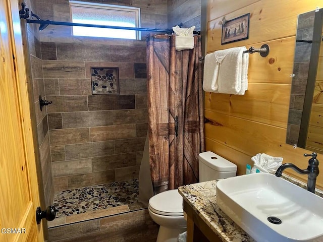 full bathroom featuring wooden walls, tiled shower, vanity, and toilet