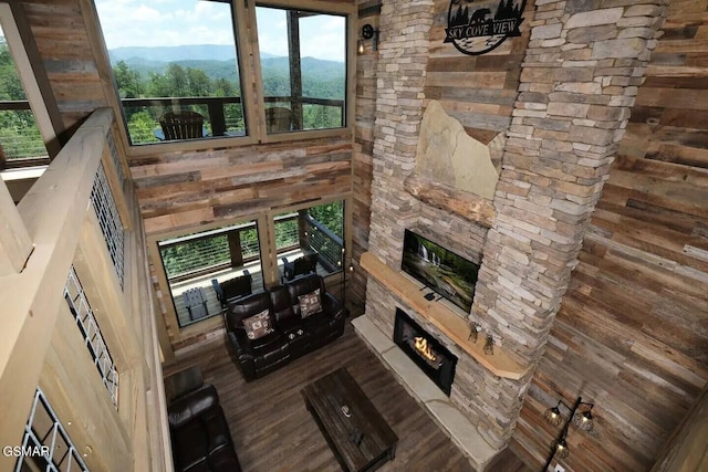 living room featuring a towering ceiling, wood walls, a mountain view, a stone fireplace, and wood finished floors