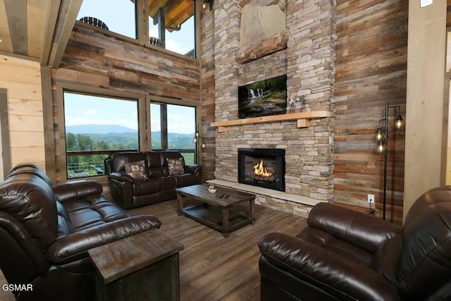 living room with beam ceiling, wood walls, a stone fireplace, and wood finished floors