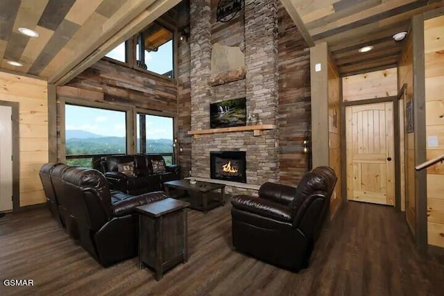 living room with a stone fireplace, wood finished floors, a towering ceiling, and wooden walls