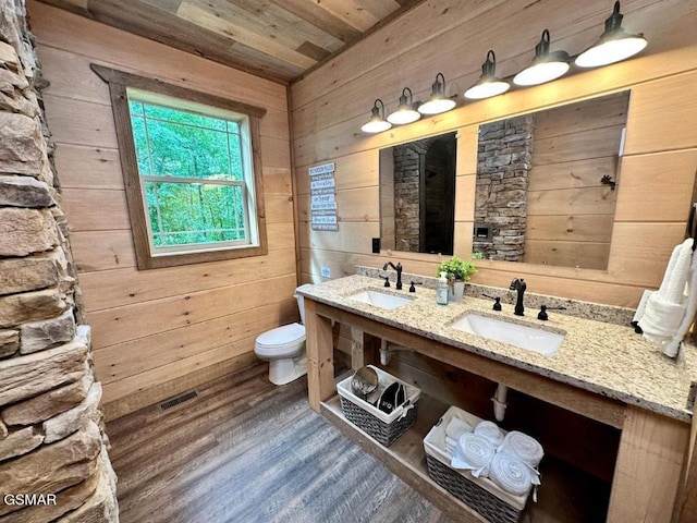 bathroom featuring wood finished floors, wood walls, a sink, and toilet