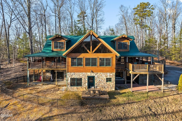 rear view of house with a wooden deck, fence private yard, metal roof, stone siding, and a patio