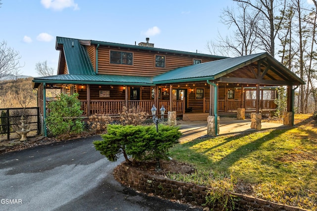 rear view of property featuring log veneer siding, a porch, a yard, metal roof, and a chimney