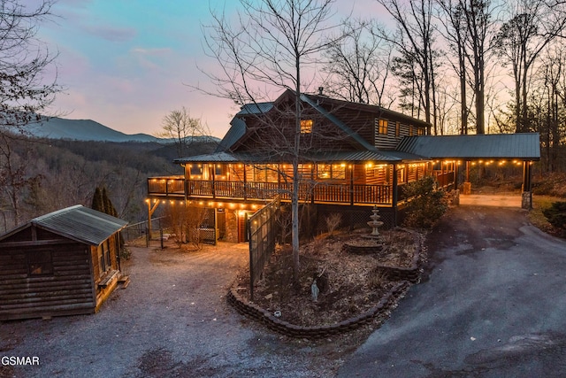 rear view of property with log veneer siding, driveway, a mountain view, an outdoor structure, and metal roof