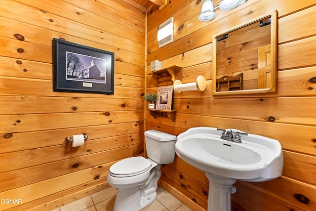 half bath with a sink, toilet, wooden walls, and tile patterned flooring