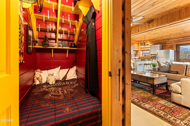 bedroom with wood walls, wooden ceiling, and freestanding refrigerator