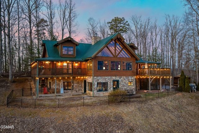 back of house at dusk with stone siding, a deck, a chimney, and a patio area