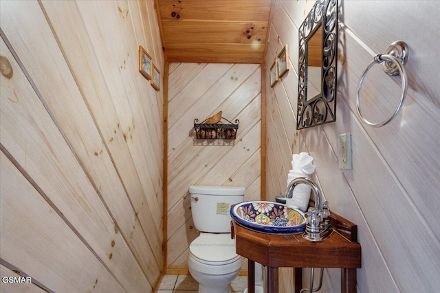 bathroom with toilet, wood walls, and tile patterned flooring