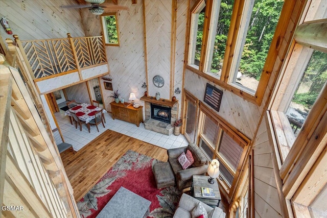 living room with a stone fireplace, wood finished floors, wood walls, and ceiling fan