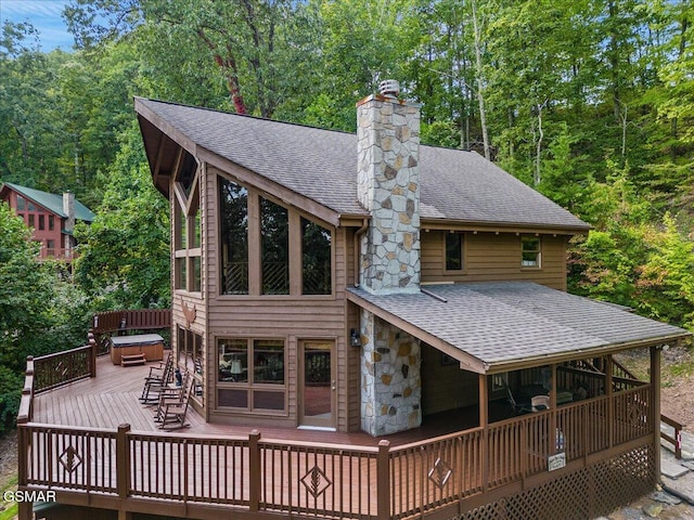 back of property featuring a wooden deck, a chimney, stone siding, and a shingled roof