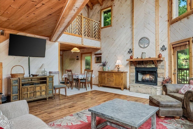 living area with beamed ceiling, wood ceiling, a stone fireplace, wood finished floors, and plenty of natural light