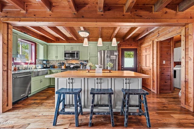 kitchen featuring a center island, green cabinetry, butcher block countertops, washer / dryer, and stainless steel appliances