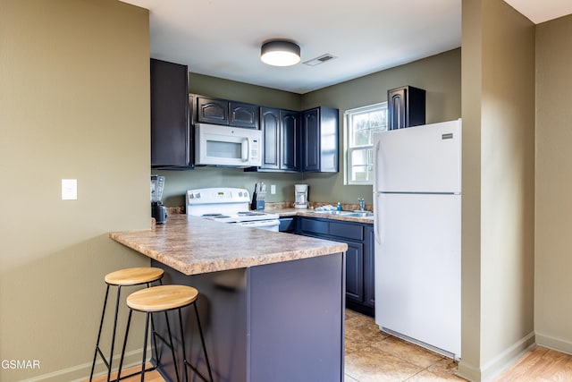 kitchen with white appliances, a peninsula, a sink, light countertops, and a kitchen breakfast bar