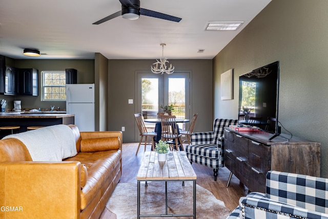 living room with ceiling fan with notable chandelier, light wood-style floors, visible vents, and a textured wall