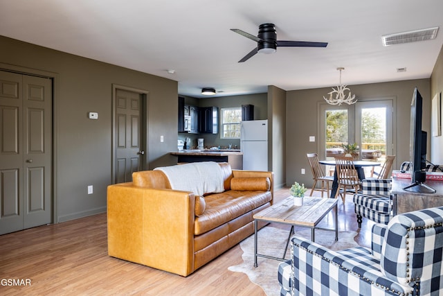 living area with visible vents, baseboards, light wood-style flooring, and ceiling fan with notable chandelier